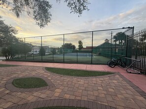 A fenced tennis court with a paved walkway and a bicycle parked by the fence. - Cozy Private Studio, 20 Minutes from Disney (Clermont)