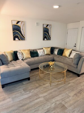 A living room with a sectional sofa, a glass coffee table, and two abstract paintings on the wall. - 1br Apartment in ATL (Atlanta)