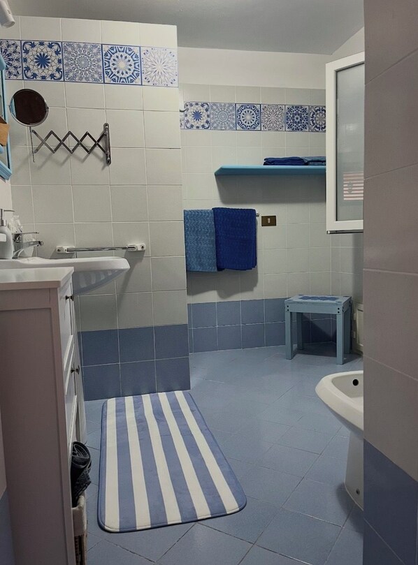 A bathroom with a sink, mirror, towel rack, and a blue and white striped bath mat. - Judy Holiday House (Sicilia)