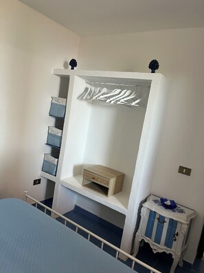 A bedroom with a bed, a white wardrobe with hanging space, a bedside table, and a blue-striped nightstand.