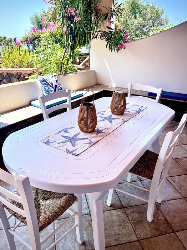 An outdoor patio with a white table and chairs, two wicker lanterns, and a blue and white patterned table runner. - Judy Holiday House (Sicilia)