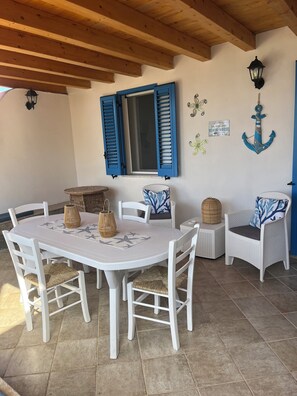 A dining area with a round table, white chairs, and blue shutters on the window.