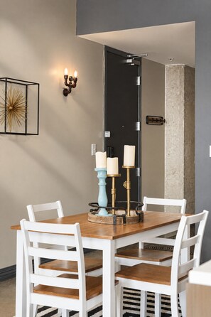 A dining area with a rectangular table, white chairs, and a wall-mounted light fixture. - The Bentley Collection - The Turquoise Loft (Dallas)