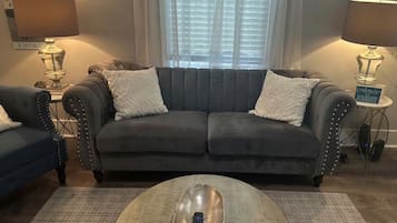 Een woonkamer met een grijze bank, twee fauteuils, een salontafel en een lamp.