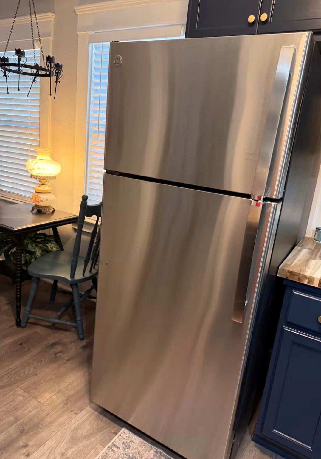 Un refrigerador de acero inoxidable en una cocina con piso de madera, una mesa de comedor y una silla.
