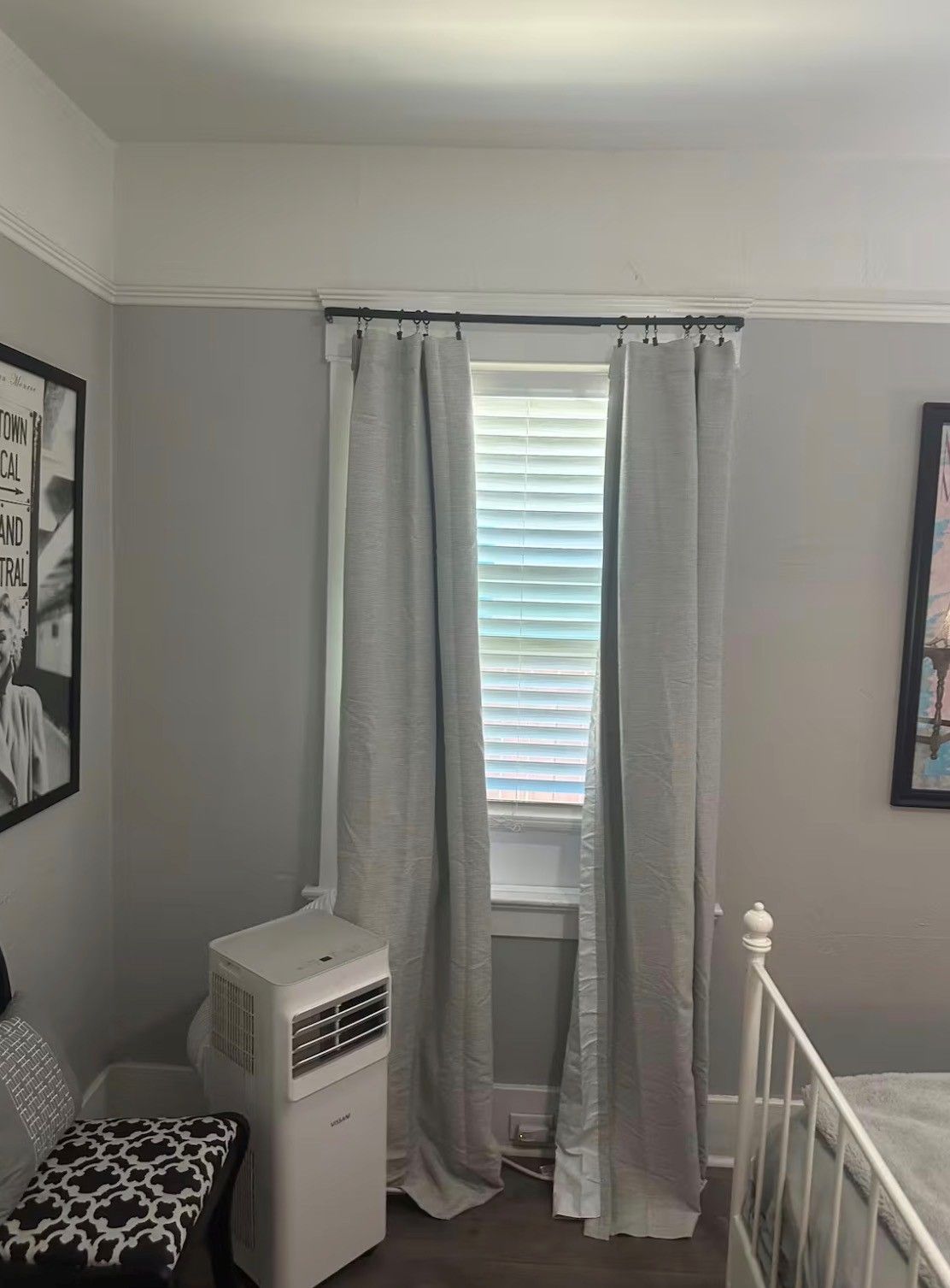 Un dormitorio con ventana, radiador, cama y un cuadro en la pared.