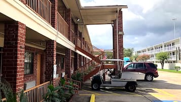 Un edificio a più piani con facciata in mattoni, un'area esterna coperta e un parcheggio con posti delimitati.