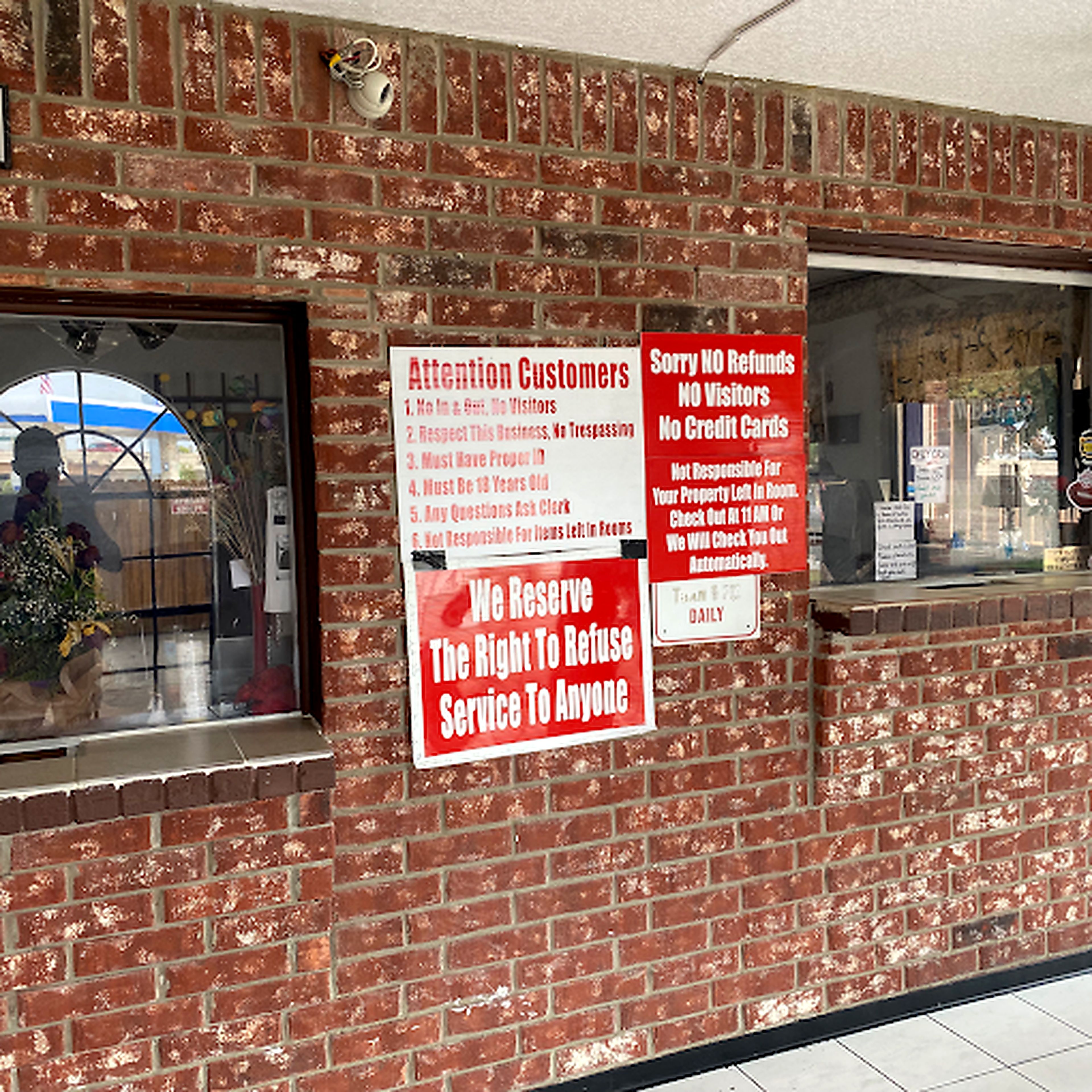 Un muro di mattoni con diversi cartelli, tra cui uno che recita 'Attenzione clienti' e un altro che indica 'Niente rimborsi, Niente visitatori, Niente carte di credito'.