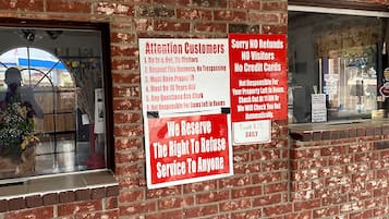 Un muro di mattoni con diversi cartelli, tra cui uno che recita 'Attenzione clienti' e un altro che indica 'Niente rimborsi, Niente visitatori, Niente carte di credito'.