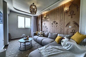 A modern living room with a grey sofa, a round coffee table, and a decorative wall with ancient Egyptian hieroglyphs. - Soul OF Pyramids Golf Epic view (Giza Governorate)