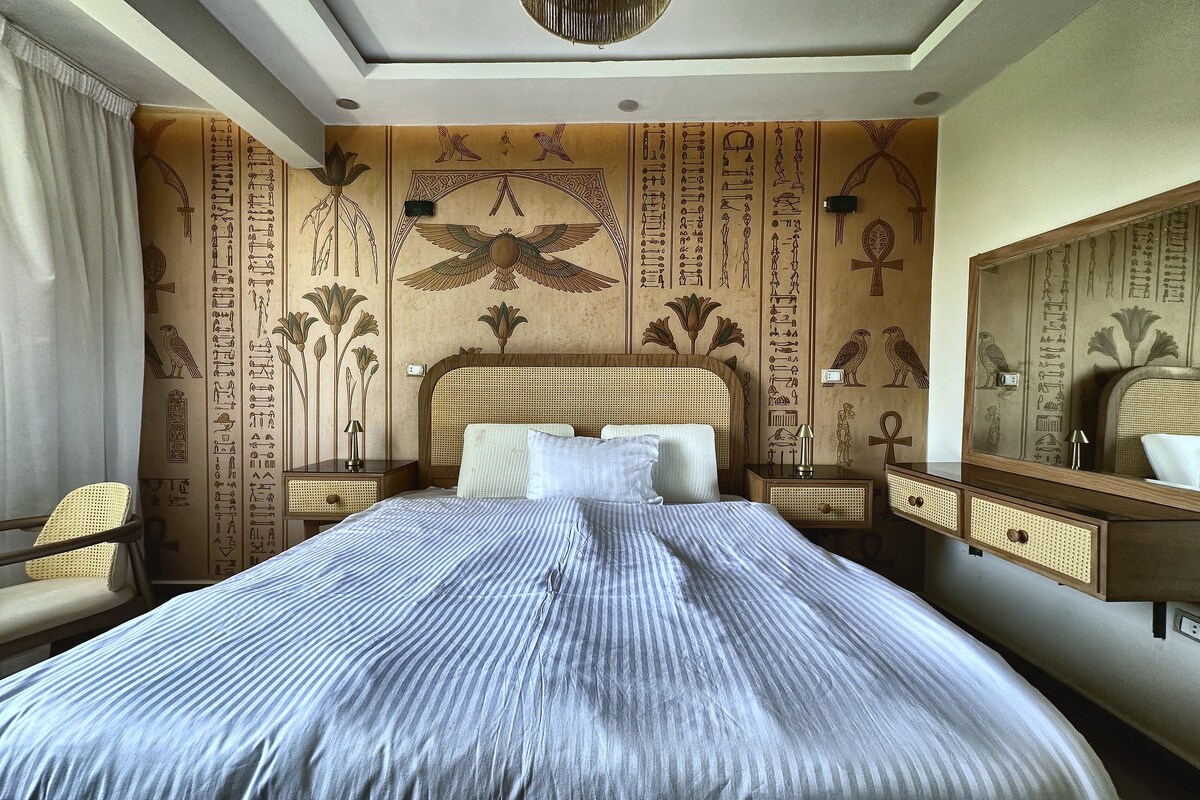 A room with a bed, a chair, a nightstand, a dresser, and a mirror.