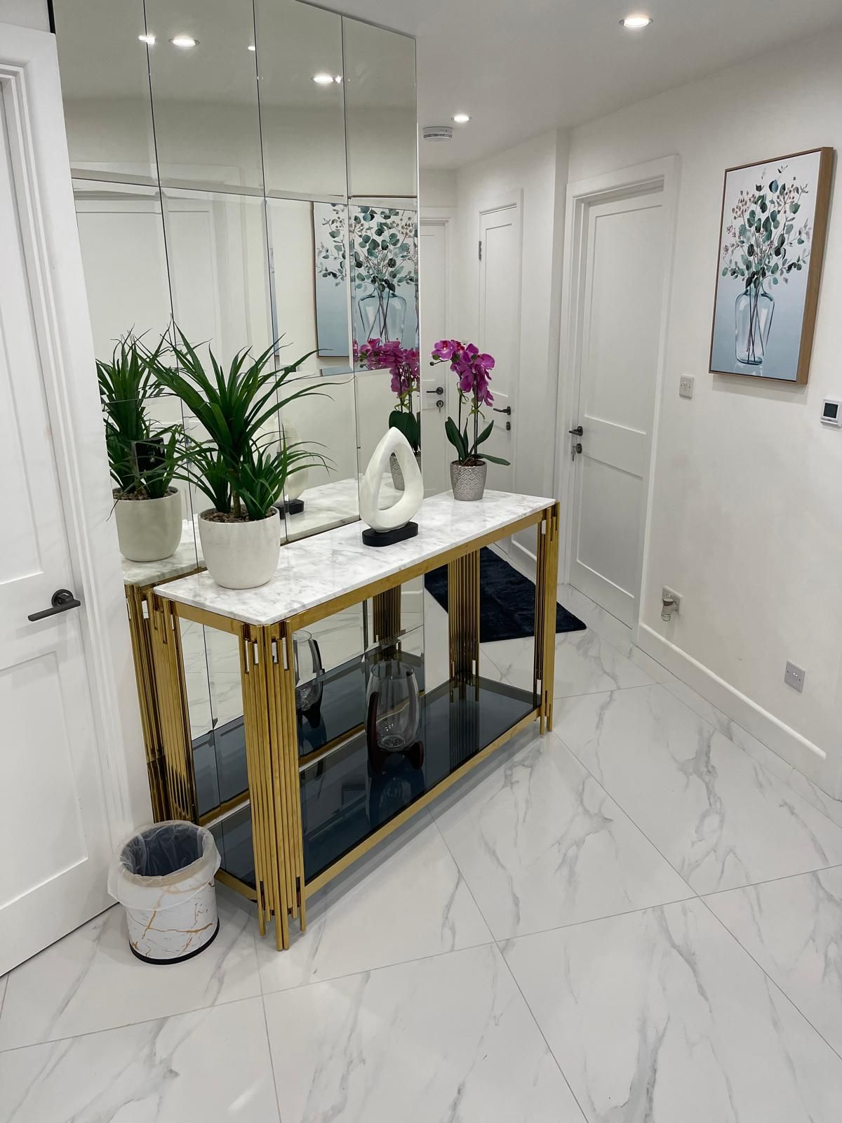 Un interior moderno con suelo de mármol, una mesita consola de cristal y plantas en macetas.