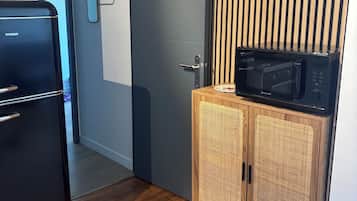 Une cuisine compacte avec un réfrigérateur noir, un meuble en bois contenant un micro-ondes et une porte donnant sur une autre pièce.