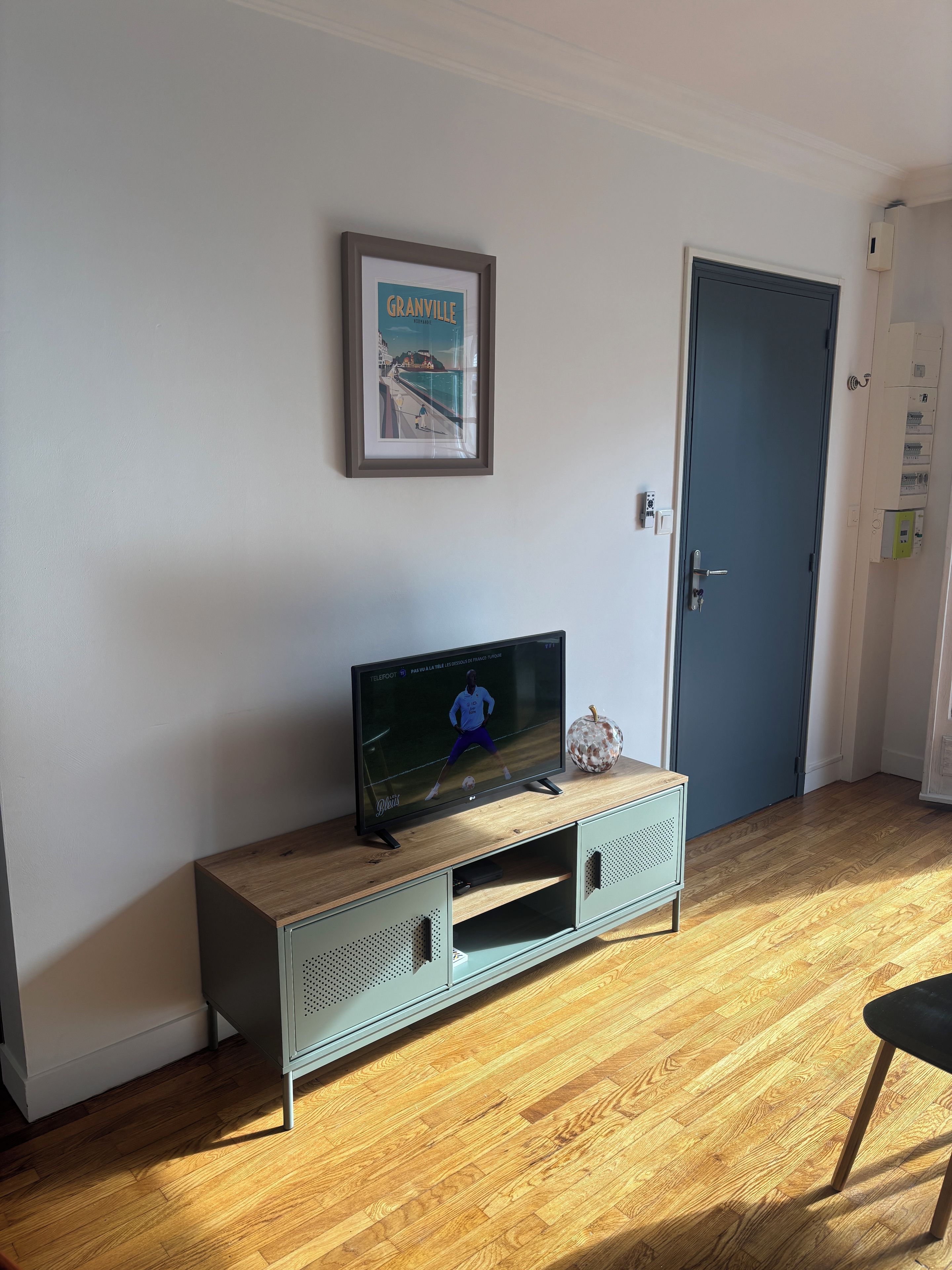 A room with a television on a wooden cabinet, a framed picture on the wall, and a door with a lock.