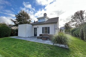 A single-story house with a brick exterior, a black door, and a small front porch with steps. - Your vacation home with a sauna and charging station on Texel – relaxation, nature, and the sea (De Cocksdorp)
