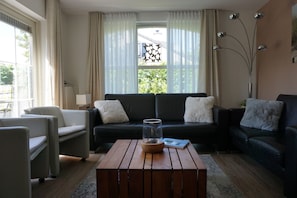 Ein Wohnzimmer mit einer Couch, Sesseln, einem Couchtisch und einem Fenster mit Vorhängen.