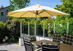 An outdoor patio with a table and chairs, a large umbrella, and a view of a house and greenery. - Your vacation home with a sauna and charging station on Texel – relaxation, nature, and the sea (De Cocksdorp)