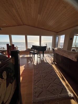 Ein geräumiges Zimmer mit einem großen Klavier, einer Couch und Meerblick durch große Fenster.