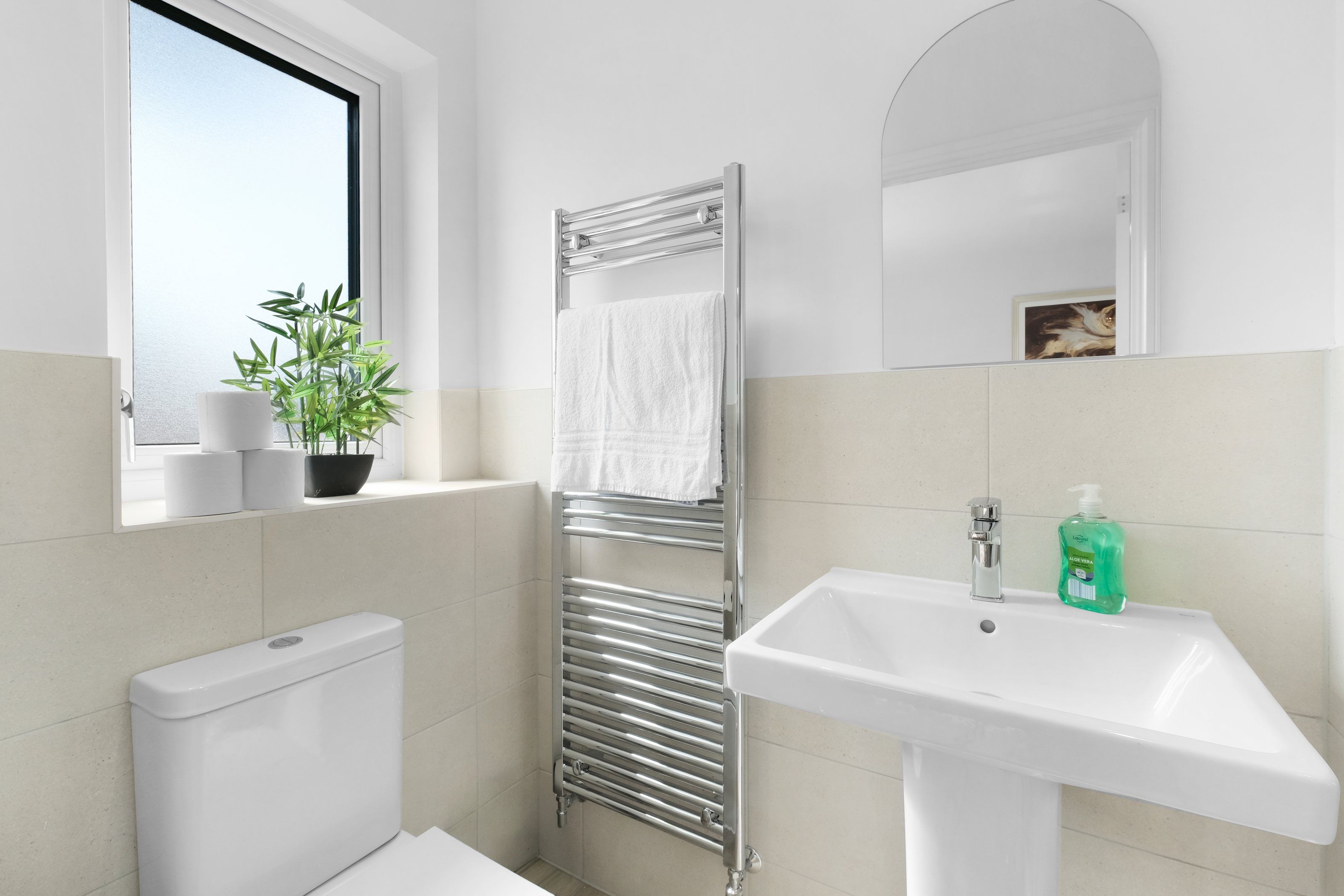 Une salle de bain moderne équipée de toilettes, d’un lavabo, d’un porte-serviettes et d’une fenêtre agrémentée d’une plante.