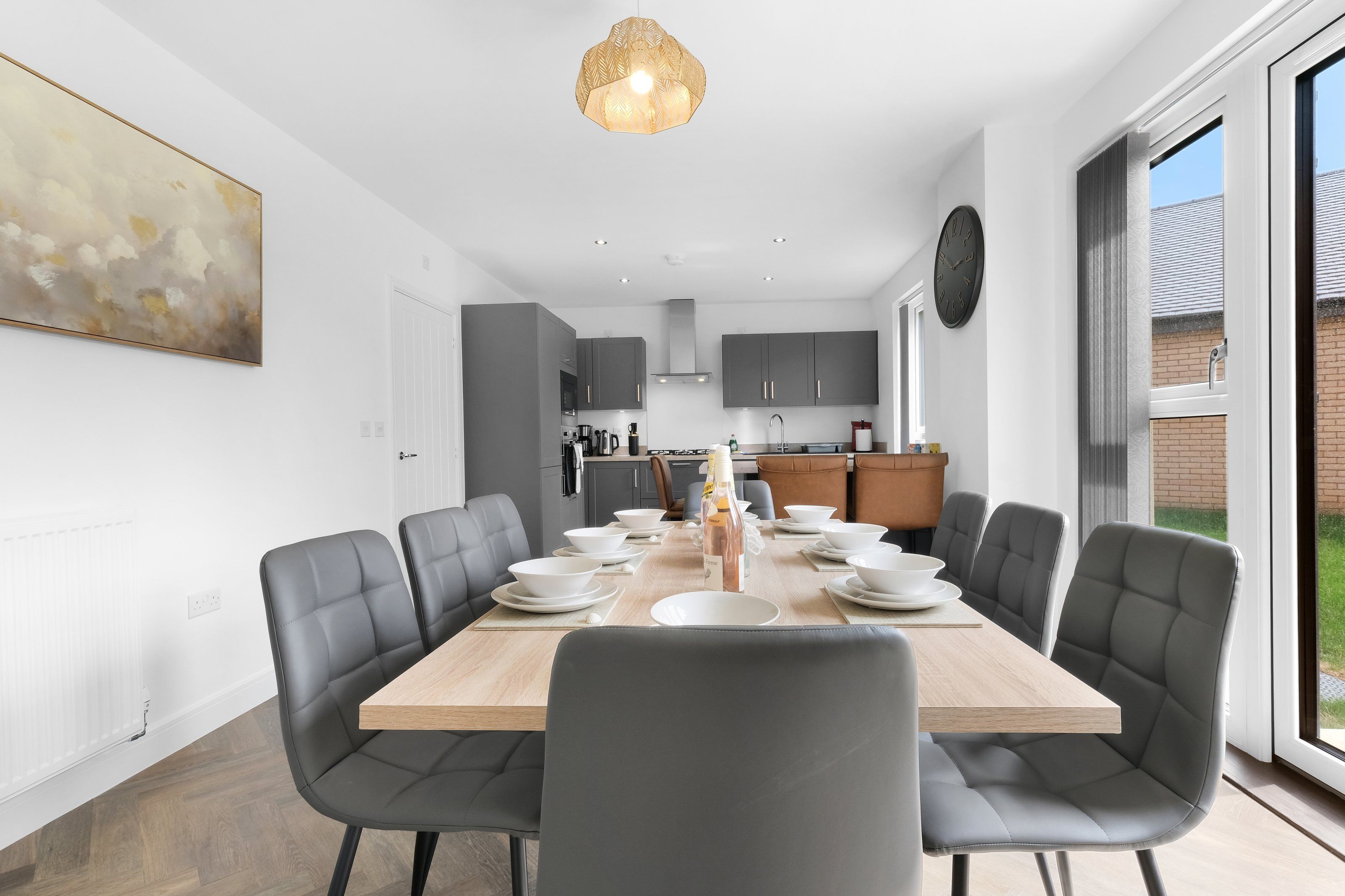 A modern dining area with a large wooden table, grey upholstered chairs, and a pendant light.