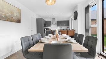 A modern dining area with a large wooden table, grey upholstered chairs, and a pendant light.