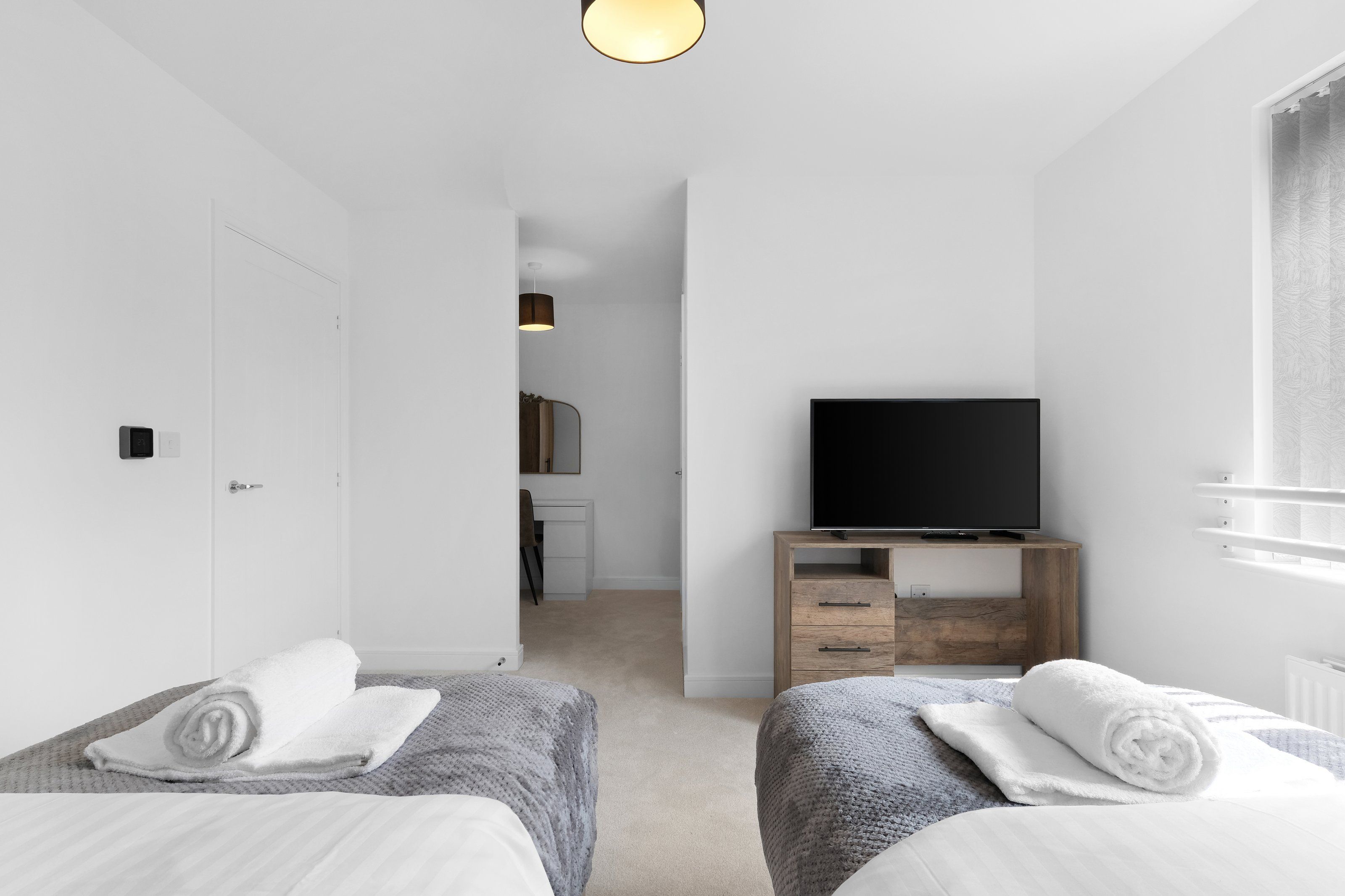 Une chambre moderne avec deux lits, un téléviseur posé sur un meuble en bois, et une salle de bain visible à travers une porte ouverte.