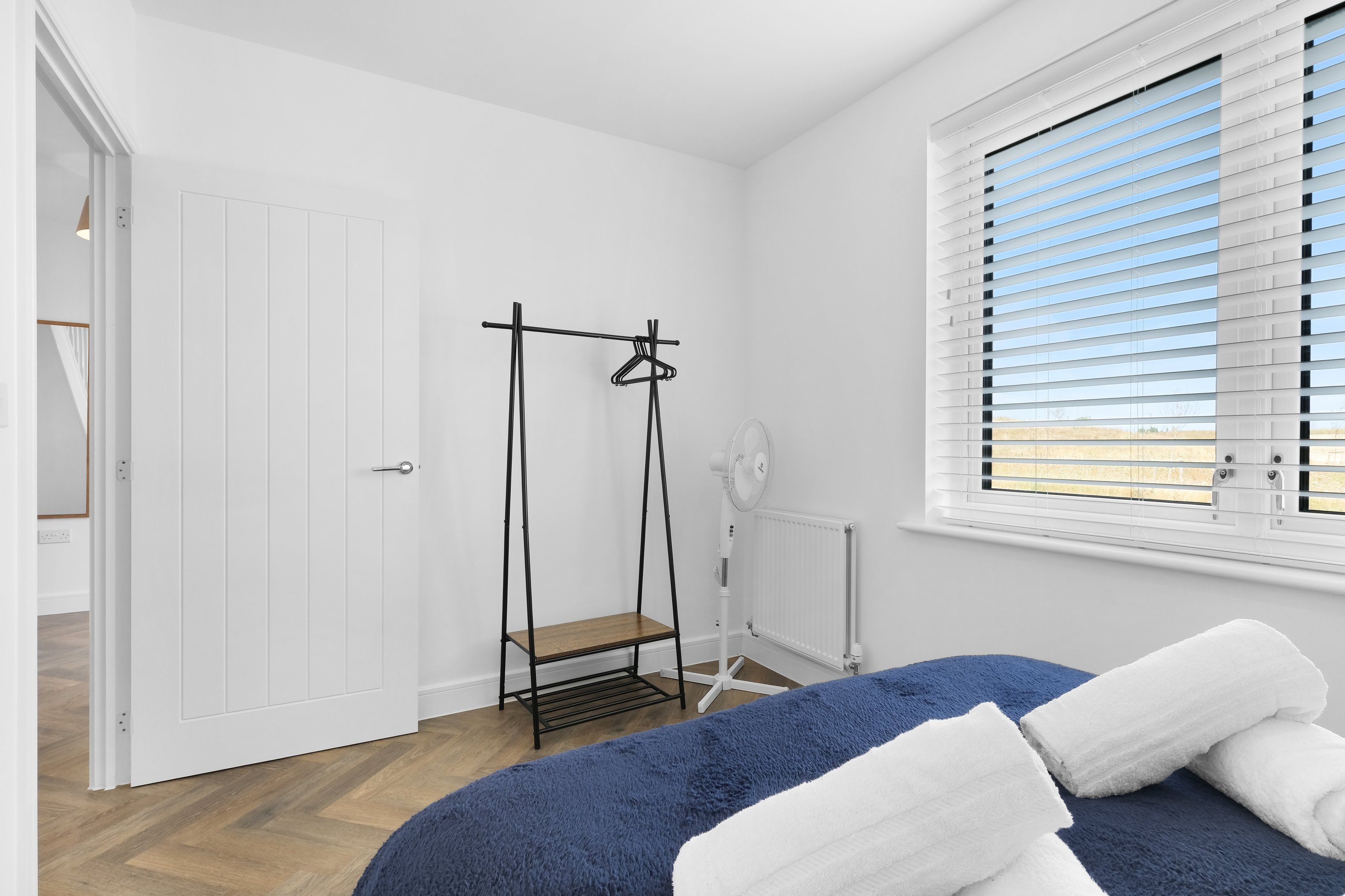 Quarto com cama, radiador, janela com persianas e porta.