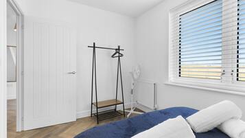 Quarto com cama, radiador, janela com persianas e porta.