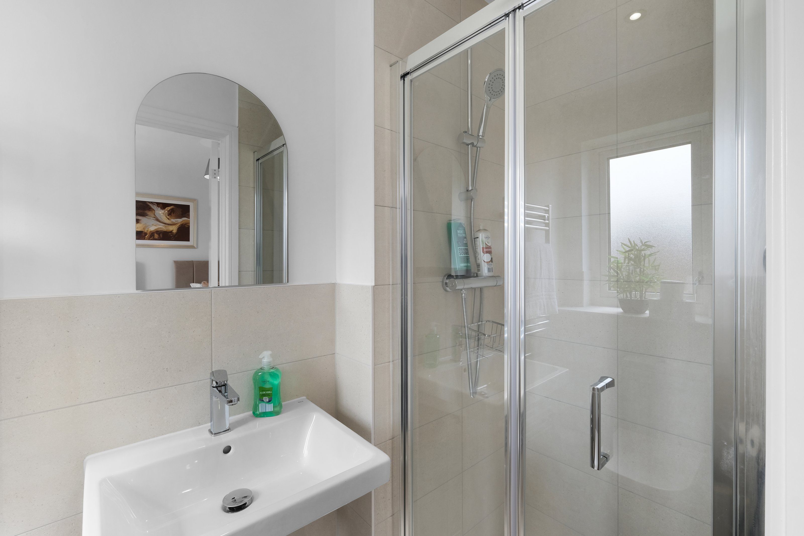 A bathroom with a glass-enclosed shower, a sink with a mirror, and toiletries.