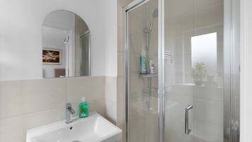 A bathroom with a glass-enclosed shower, a sink with a mirror, and toiletries.