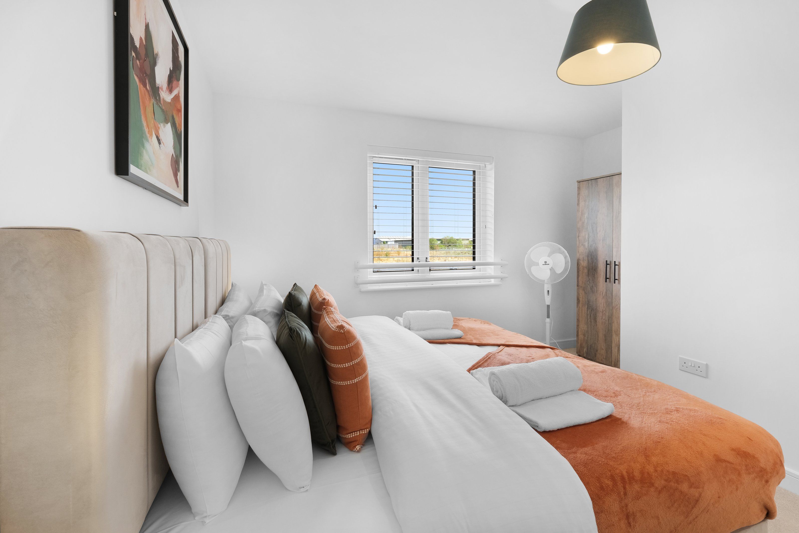 A bedroom with a bed, pillows, a window, a fan, and a wardrobe.