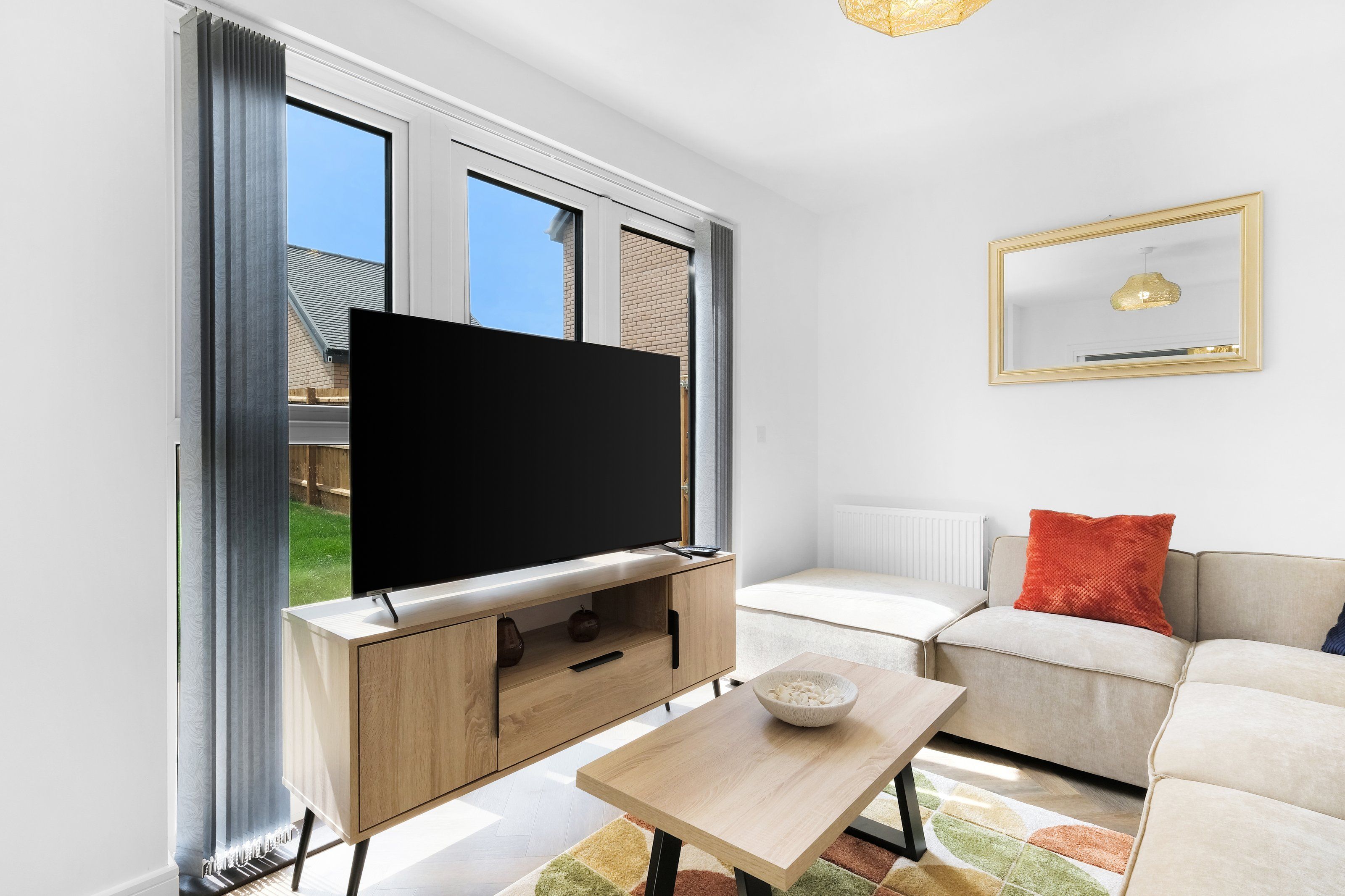 Una sala moderna con un televisor de pantalla plana sobre un mueble de madera, un sofá color beige y una pequeña mesa con un cuenco.