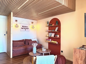 A modern living room with a wooden ceiling, a red sofa, a bookshelf, and a small round table.