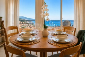 A round dining table with white plates and bowls, set with cutlery, and a vase of white flowers. - Monaco Luxury Apartment • Terrace • Parking • Sleeps 5. View of Monaco (Beausoleil)