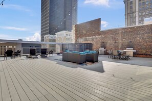 A rooftop terrace with outdoor seating, a brick wall, and modern buildings in the background. - PremiumStays: Luxury 2bd loft apt w/ Balcony : ADA : Theater : Arena : Parking (Cleveland)