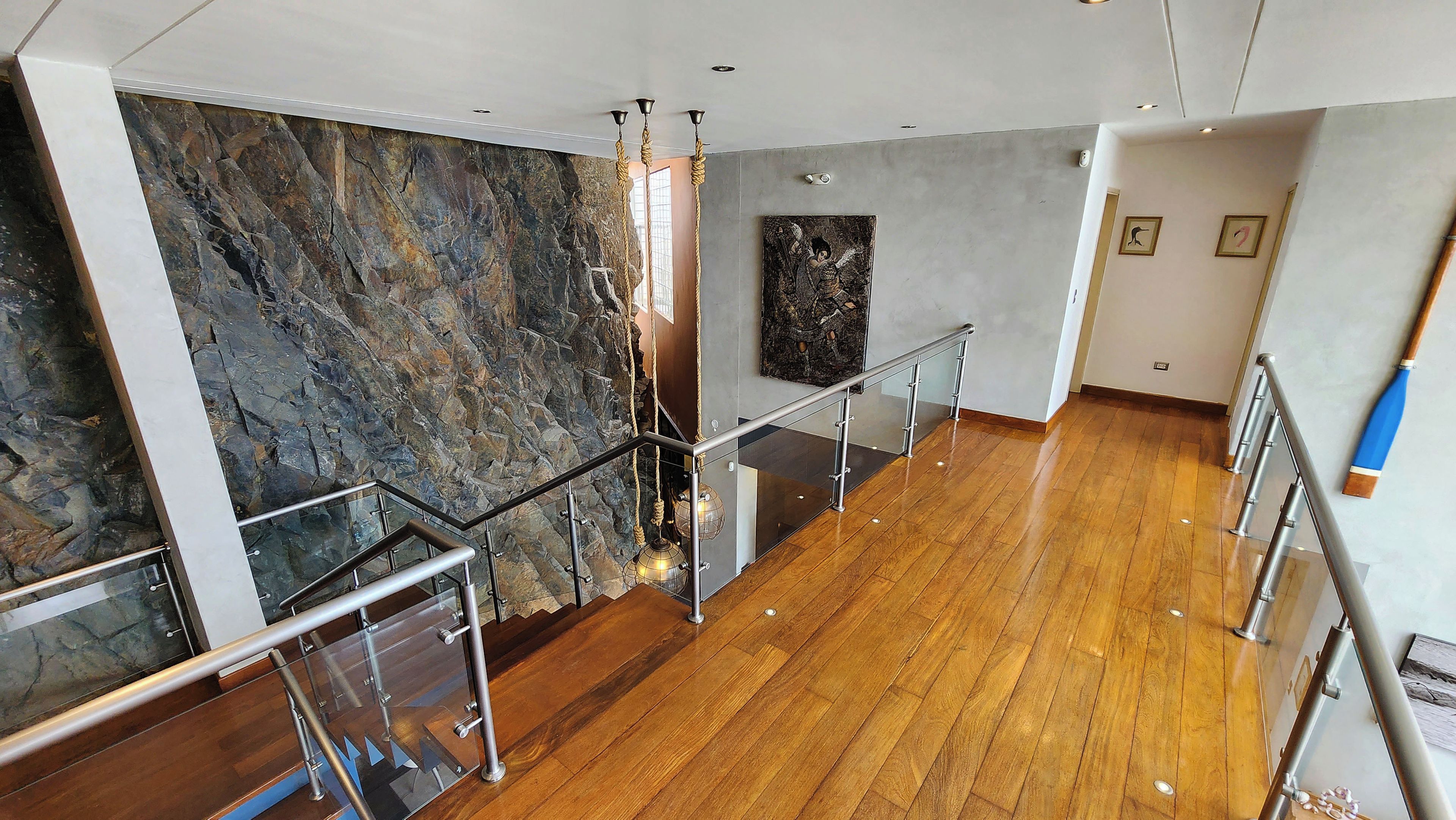 Un intérieur moderne avec un plancher en bois, une rambarde en verre et un mur en pierre.