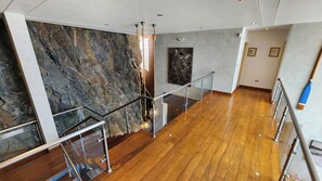 Un intérieur moderne avec un plancher en bois, une rambarde en verre et un mur en pierre.