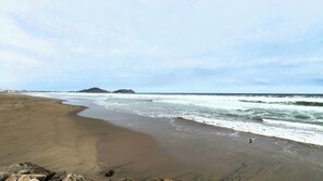 A beach with a sandy shore, waves, and distant hills.