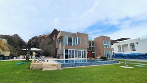A modern two-story house with a swimming pool, a balcony, and a view of a rocky hillside.