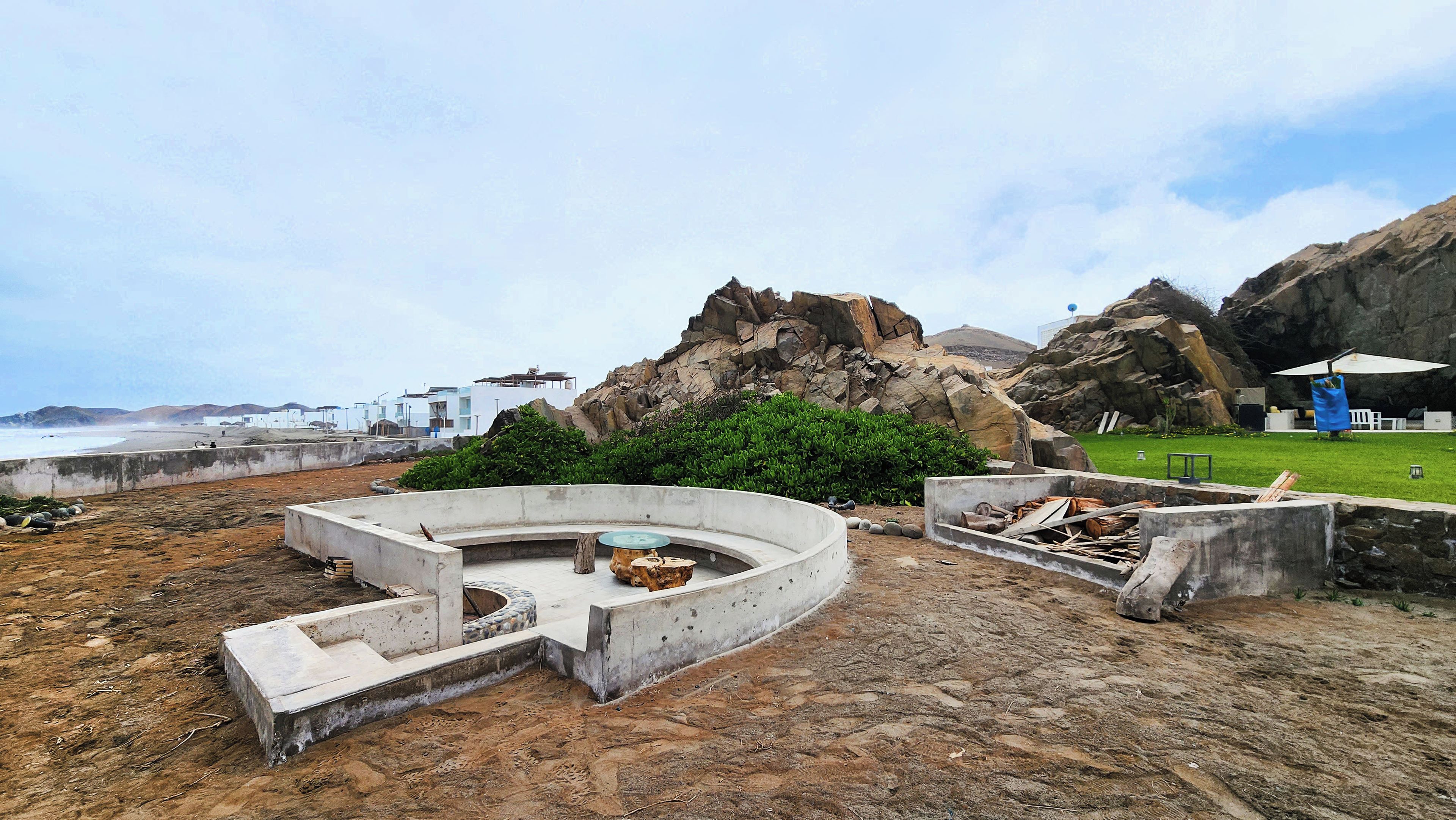 Un espace de détente en béton, de forme circulaire, avec une pelouse verdoyante et un terrain rocheux.