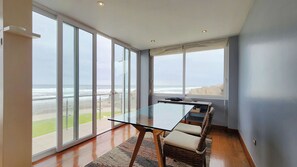 A modern room with a glass table, a wicker chair, and a view of the ocean.