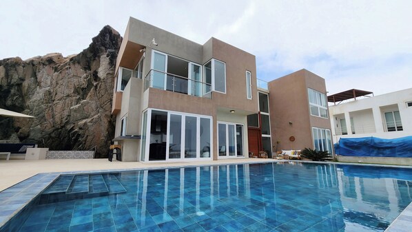 A modern building with a pool, large windows, and a rock formation.