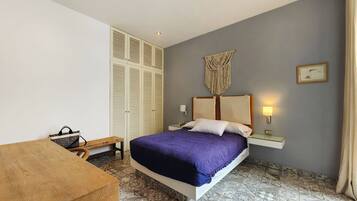 Une chambre à coucher avec un lit, des lampes de chevet, une armoire, un banc et une décoration murale en macramé.