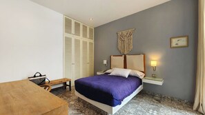 Une chambre à coucher avec un lit, des lampes de chevet, une armoire, un banc et une décoration murale en macramé.