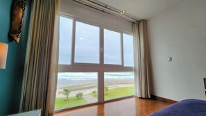 A room with a large window offering a view of the beach and ocean.
