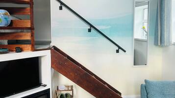 Un salon moderne avec un escalier en bois, une cheminée, un canapé bleu et une fresque murale.