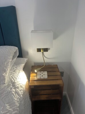 Een nachtkastje met een lamp, een stopcontact en een houten plankje.