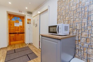 A kitchen area with a microwave on a cabinet, a wooden door, and a stone wall. - Fantastic 2-bedroom apartment in the heart of vibrant Budapest. (Budapest)