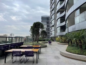 A rooftop terrace with outdoor seating and a view of a modern building. - Brooklin New Style | Complete, Carrefour 24h and Brooklin Metro, Swimming Pool and Gym (São Paulo)