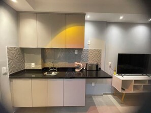 A modern kitchen with a black countertop, a built-in oven, a coffee maker, and a flat-screen TV. - Brooklin New Style | Complete, Carrefour 24h and Brooklin Metro, Swimming Pool and Gym (São Paulo)